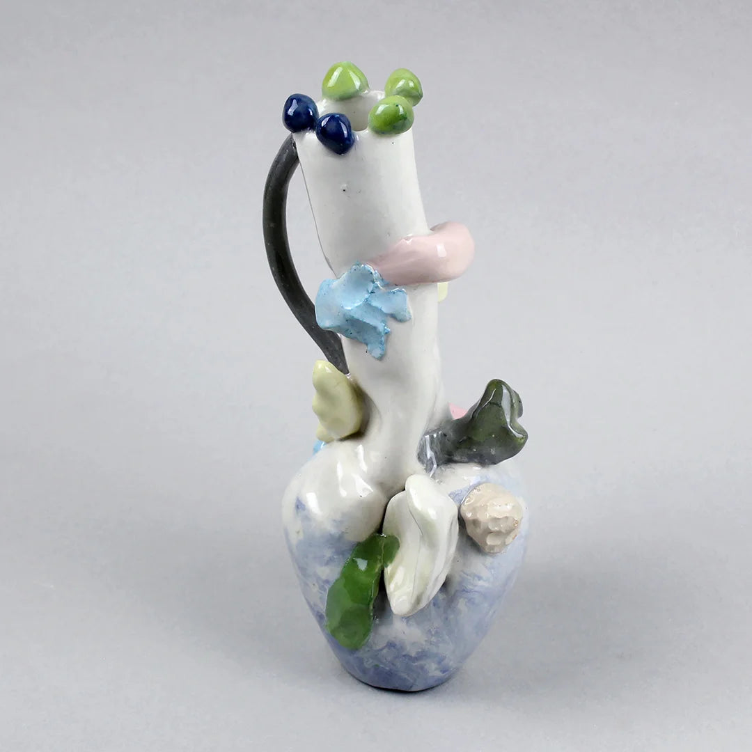 Hand-built decorative ceramic jar with organic, abstract forms and colourful details, made from earthenware and coloured earthenware, finished with a glossy transparent glaze. Created by artist Cíntia Coutinho, also known as Espirro, and photographed on a grey background.