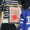 Hanging clothes with a tile with an illustration of a red apple and green leaves on a wooden rack.