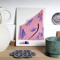 Wall object with an illustration of a pink mountain on a wooden surface with decorative items around