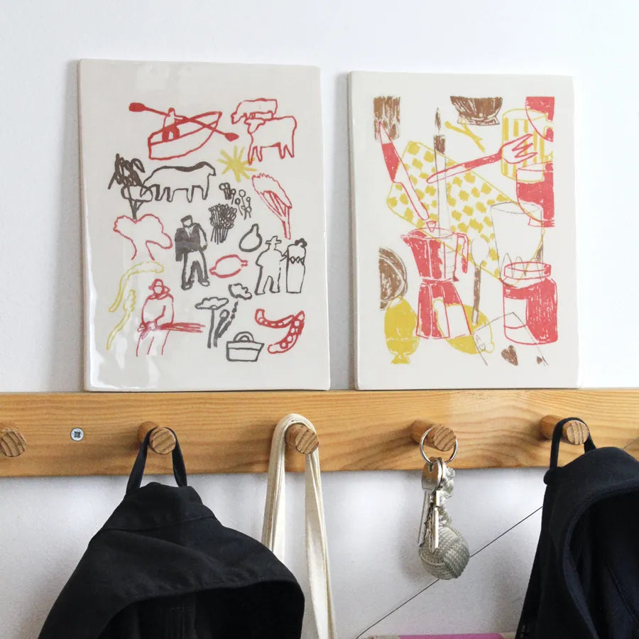 Two wall objects with abstract designs above a wooden coat rack with hooks.