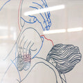 Detail of a manual screen print (50×70 cm) of an illustration of Tina Siuda showing two bodies embracing, drawn with fine linework on a white background. The figures extend almost to the edges of the paper, as if confined within its borders. The print is framed in a grey frame and hung on a Klein blue wall with matching blue metal bars.