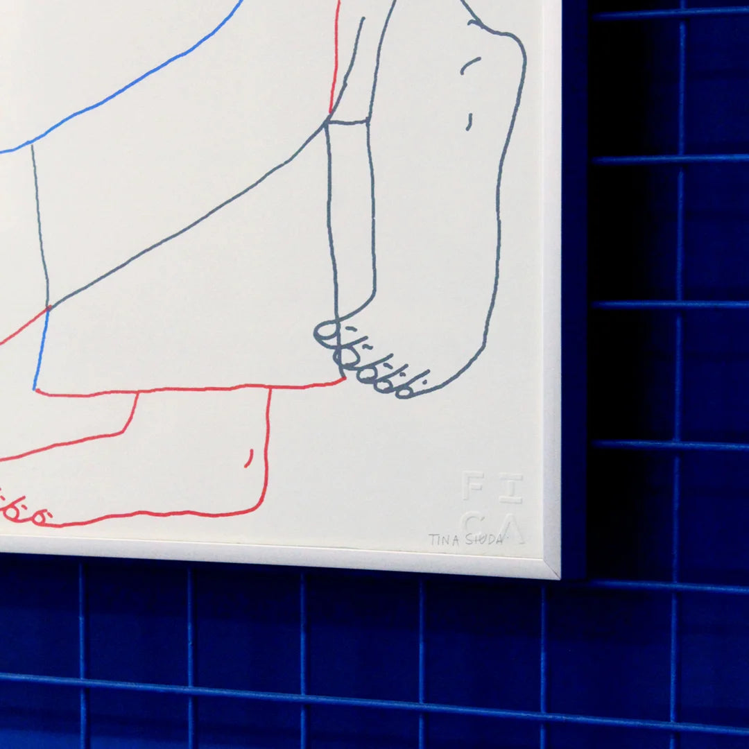 Detail of a Manual screen print (50×70 cm) of an illustration showing two bodies embracing, drawn with fine linework on a white background. The figures extend almost to the edges of the paper, as if confined within its borders. The print is framed in a grey frame and hung on a Klein blue wall with matching blue metal bars.