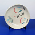 Hand-built decorative ceramic deep plate with organic, abstract forms and colourful details, made from earthenware and coloured earthenware, finished with a glossy transparent glaze. Created by artist Cíntia Coutinho, also known as Espirro.