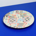 Hand-built decorative ceramic plate with organic, abstract forms and colourful details, made from earthenware and coloured earthenware, finished with a glossy transparent glaze. Created by artist Cíntia Coutinho, also known as Espirro.
