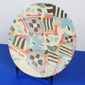 Hand-built decorative ceramic plate with organic, abstract forms and colourful details, made from earthenware and coloured earthenware, finished with a glossy transparent glaze. Created by artist Cíntia Coutinho, also known as Espirro.