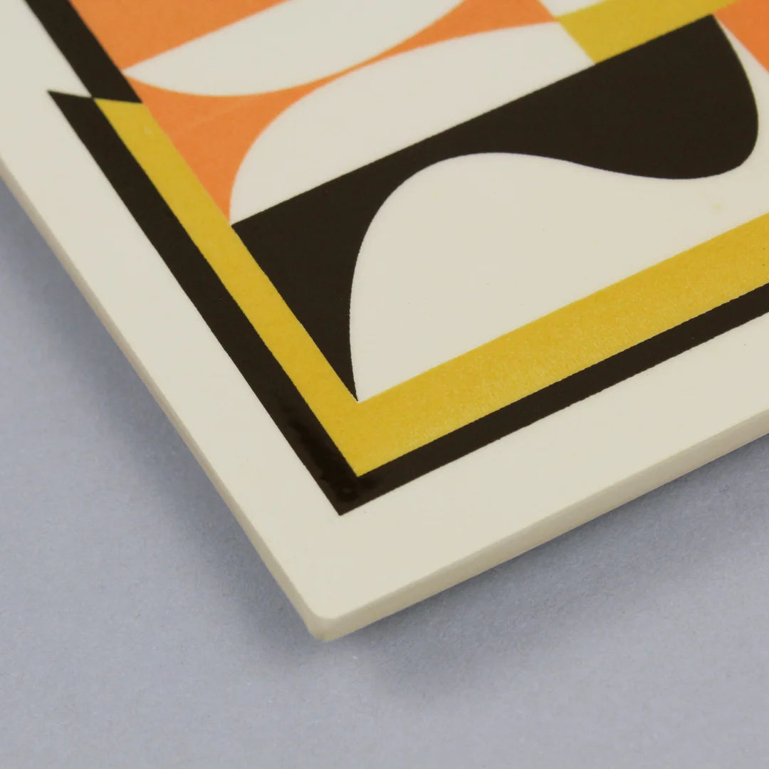 Detail of a screen-printed tile with an Artwork from Luís Silva, with orange, yellow and black colors, on a stand against a gray background