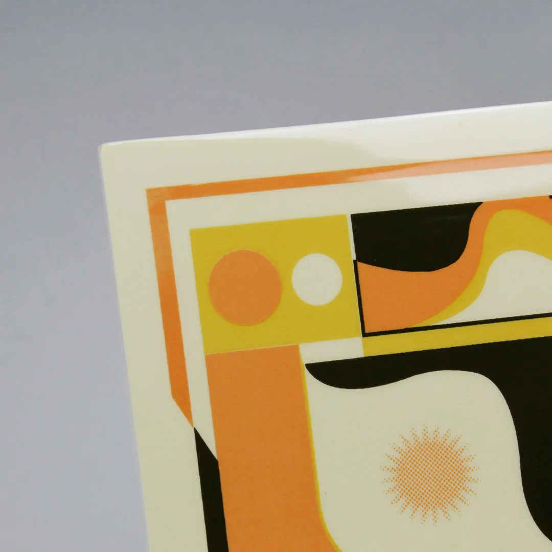 Detail of a screen-printed tile with an Artwork from Luís Silva, with orange, yellow and black colors, on a stand against a gray background