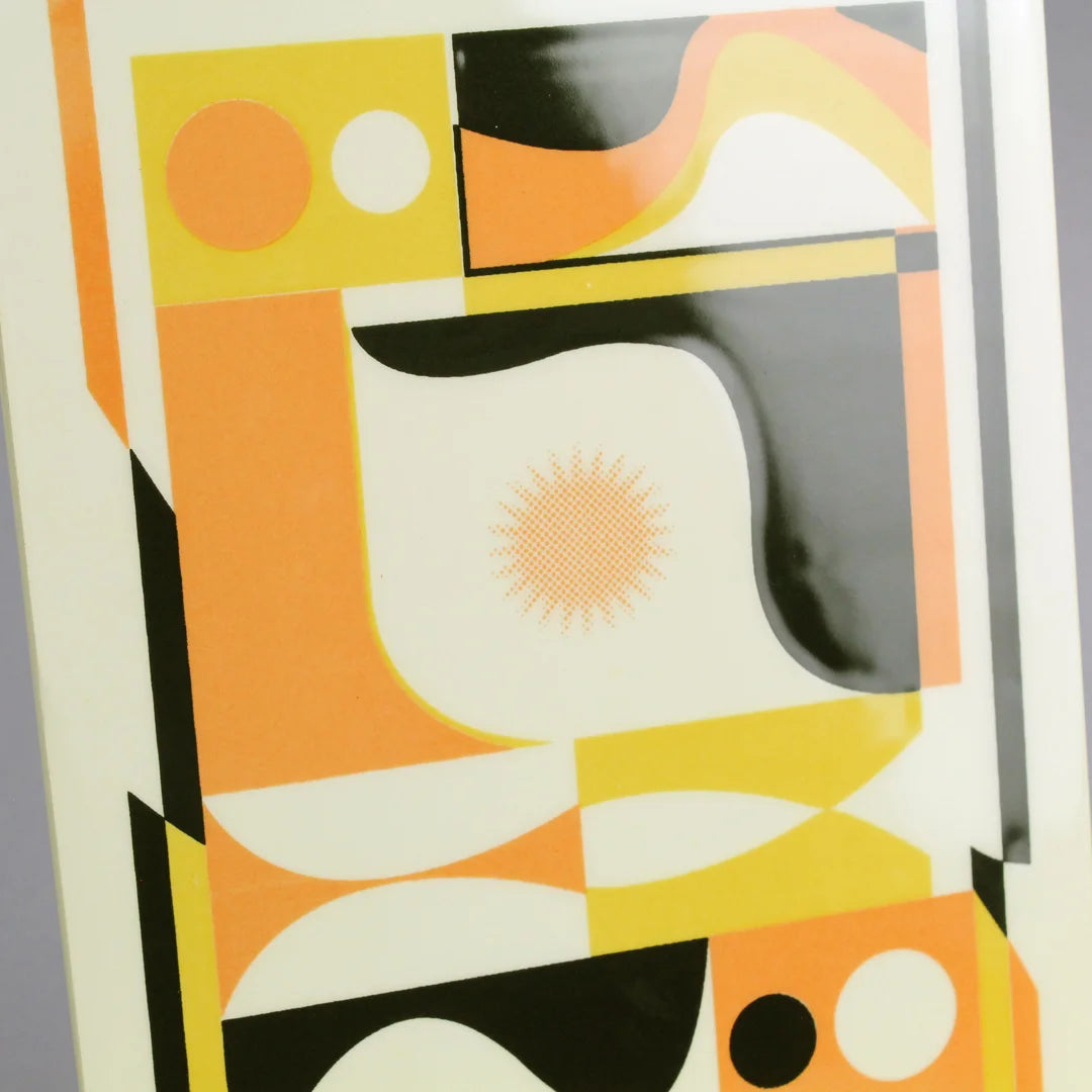 Screen-printed tile with an Artwork from Luís Silva, with orange, yellow and black colors, on a stand against a gray background
