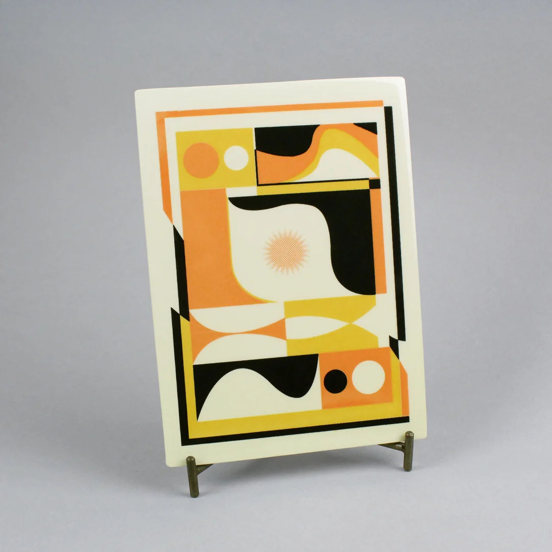 Screen-printed tile with an Artwork from Luís Silva, with orange, yellow and black colors, on a stand against a gray background
